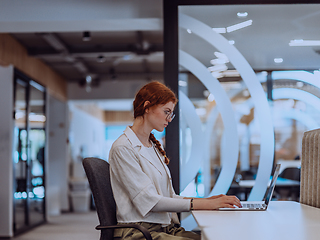 Image showing A young businesswoman with orange hair sitting confidently, fully engaged in her work on the laptop, exuding creativity, ambition, and a vibrant sense of individuality