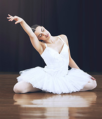 Image showing Ballerina sitting on the floor in a studio or on a stage, in a pose during dance. Young ballet dancer with her hand up while dancing or posing during theatre performance of beauty, grace and elegant