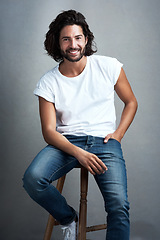 Image showing Fashion, smile and portrait of man in studio on a stool with casual, cool and stylish outfit. Happy, handsome and confident young male model from Mexico with trendy style on chair by gray background.