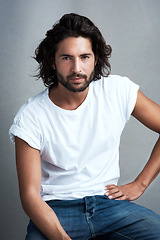 Image showing Style, serious and portrait of man in studio on a stool with casual, cool and stylish outfit. Confidence, handsome and young male model from Mexico with trendy clothes on chair by gray background.