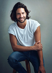 Image showing Fashion, smile and portrait of man in studio on a stool with casual, cool and stylish outfit. Happy, handsome and confident young male model from Mexico with trendy style on chair by gray background.