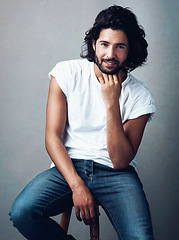 Image showing Fashion, handsome and portrait of man in studio on a stool with casual, cool and stylish outfit. Happy, smile and confident young male model from Mexico with trendy style on chair by gray background.