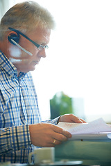 Image showing Man, paperwork and headset for communication in office for career in telesales, customer care or tech support. Mature agent, call centre and document for reading, review or report for consumer growth