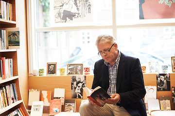 Image showing Senior man, library and reading book for literature, knowledge or story at bookstore. Mature male person, author or bookworm sitting by bookshelf for novel, learning or wisdom in shopping or leisure