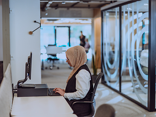 Image showing In a modern office, a young Muslim entrepreneur wearing a hijab sits confidently and diligently works on her computer, embodying determination, creativity, and empowerment in the business world