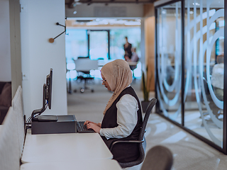 Image showing In a modern office, a young Muslim entrepreneur wearing a hijab sits confidently and diligently works on her computer, embodying determination, creativity, and empowerment in the business world