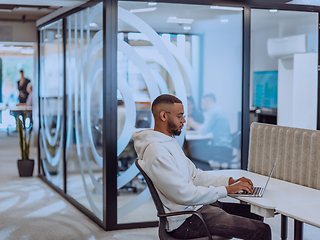 Image showing In a modern office setting, an African American businessman is diligently working on his laptop, embodying determination, ambition, and productivity in his professional environmen