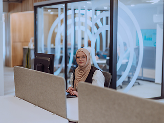 Image showing In a modern office, a young Muslim entrepreneur wearing a hijab sits confidently and diligently works on her computer, embodying determination, creativity, and empowerment in the business world