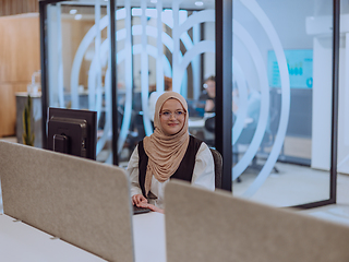 Image showing In a modern office, a young Muslim entrepreneur wearing a hijab sits confidently and diligently works on her computer, embodying determination, creativity, and empowerment in the business world