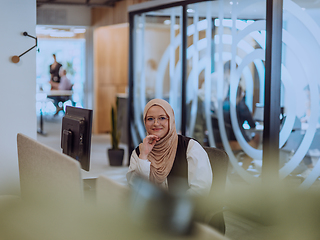 Image showing In a modern office, a young Muslim entrepreneur wearing a hijab sits confidently and diligently works on her computer, embodying determination, creativity, and empowerment in the business world