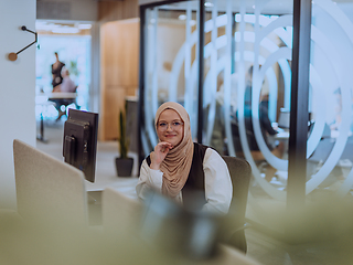 Image showing In a modern office, a young Muslim entrepreneur wearing a hijab sits confidently and diligently works on her computer, embodying determination, creativity, and empowerment in the business world