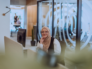 Image showing In a modern office, a young Muslim entrepreneur wearing a hijab sits confidently and diligently works on her computer, embodying determination, creativity, and empowerment in the business world