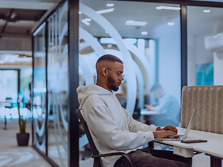 Image showing In a modern office setting, an African American businessman is diligently working on his laptop, embodying determination, ambition, and productivity in his professional environmen