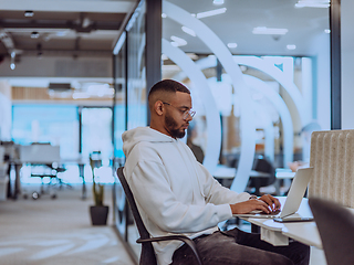 Image showing In a modern office setting, an African American businessman is diligently working on his laptop, embodying determination, ambition, and productivity in his professional environmen