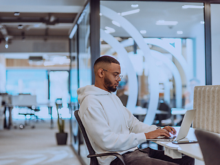 Image showing In a modern office setting, an African American businessman is diligently working on his laptop, embodying determination, ambition, and productivity in his professional environmen