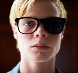 Image showing Student, man and broken sunglasses for fashion isolated on brown background in studio. Portrait, glasses and serious, young and blonde person with shades for vision, style or cool face in Switzerland
