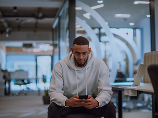 Image showing African American businessman wearing headphones while using a smartphone, fully engaged in his work at a modern office, showcasing focus, productivity, and contemporary professionalism