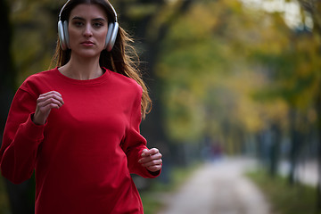 Image showing Young beautiful woman running in autumn park and listening to music with headphones on smartphone