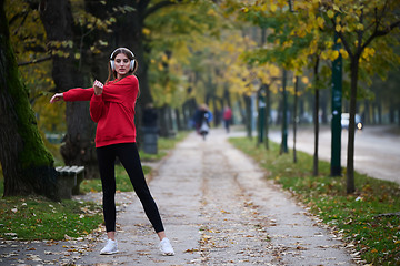 Image showing Young beautiful woman running in autumn park and listening to music with headphones on smartphone