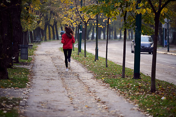 Image showing Young beautiful woman running in autumn park and listening to music with headphones on smartphone