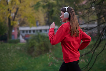 Image showing Young beautiful woman running in autumn park and listening to music with headphones on smartphone