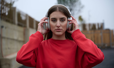 Image showing Portrait of running woman after jogging in the park on autumn seasson. Female fitness model training outside on a cozy fall day and listening to music over smartphone.