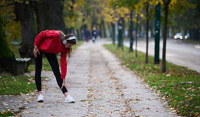 Image showing Athletic young woman taking a breath and relaxing after jogging and stretching. Woman Training and Workout Exercises On Street.