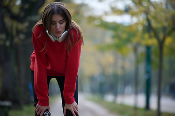 Image showing Athletic young woman taking a breath and relaxing after jogging and stretching. Woman Training and Workout Exercises On Street.