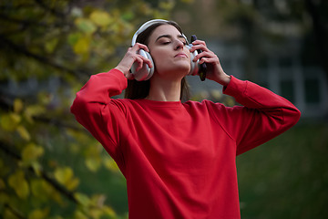Image showing Portrait of running woman after jogging in the park on autumn seasson. Female fitness model training outside on a cozy fall day and listening to music over smartphone.