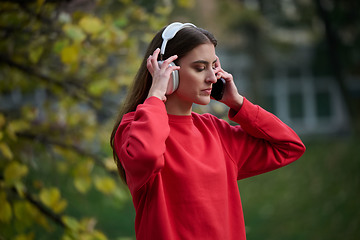 Image showing Portrait of running woman after jogging in the park on autumn seasson. Female fitness model training outside on a cozy fall day and listening to music over smartphone.