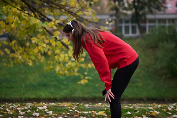 Image showing Athletic young woman taking a breath and relaxing after jogging and stretching. Woman Training and Workout Exercises On Street.