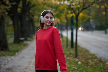 Image showing Portrait of running woman after jogging in the park on autumn seasson. Female fitness model training outside on a cozy fall day and listening to music over smartphone.