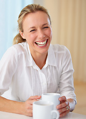 Image showing Happy mature woman, laughing and coffee for funny joke, conversation or humor on kitchen table at home. Blonde female person smile or laugh with cup of tea for meme, discussion or fun chat at house