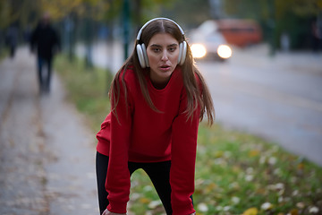 Image showing Athletic young woman taking a breath and relaxing after jogging and stretching. Woman Training and Workout Exercises On Street.