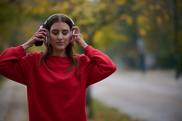 Image showing Portrait of running woman after jogging in the park on autumn seasson. Female fitness model training outside on a cozy fall day and listening to music over smartphone.