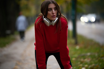 Image showing Athletic young woman taking a breath and relaxing after jogging and stretching. Woman Training and Workout Exercises On Street.