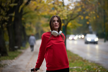 Image showing Portrait of running woman after jogging in the park on autumn seasson. Female fitness model training outside on a cozy fall day and listening to music over smartphone.