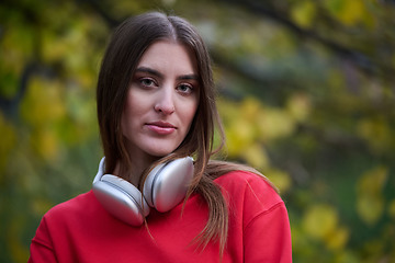 Image showing Portrait of running woman after jogging in the park on autumn seasson. Female fitness model training outside on a cozy fall day and listening to music over smartphone.