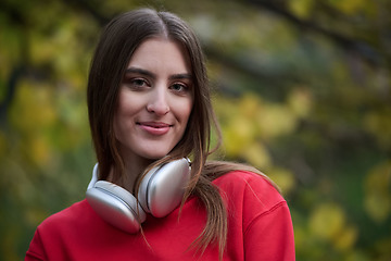 Image showing Portrait of running woman after jogging in the park on autumn seasson. Female fitness model training outside on a cozy fall day and listening to music over smartphone.