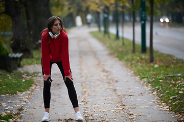 Image showing Athletic young woman taking a breath and relaxing after jogging and stretching. Woman Training and Workout Exercises On Street.