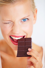 Image showing Portrait, woman wink and eating chocolate bar, delicious snack or candy for studio food, dessert or sugar product. Diet craving, cacao sweets or girl face with cheat meal isolated on white background