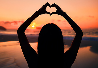 Image showing Woman, silhouette and sunset at beach with heart hands for love, care and kindness with sign, summer and dusk. Girl, person and ocean with symbol, emoji or icon on vacation, nature or outdoor in dark