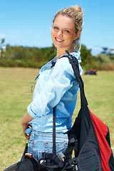 Image showing Woman, portrait or smile outdoor with grass, bags and casual fashion for travel or vacation with blue sky. Person, face or tourist and happy in nature for adventure, holiday or parachute experience