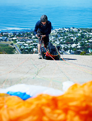 Image showing Man, parachute and paragliding sport in launch on hill, healthy adventure and extreme fitness by ocean. Person, preparation and fearless by bench for flight with helmet and safety gear by blue sky