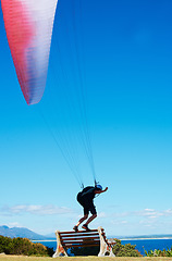Image showing Man, parachute or paragliding sport in launch exercise, healthy adventure or extreme fitness for wellness. Person, preparation and fearless by bench for flight with helmet and safety gear by blue sky
