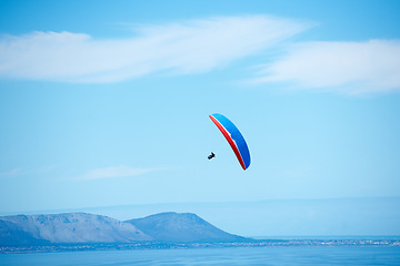 Image showing Pilot, parachute and paragliding in blue sky for flight, freedom and courage with extreme sport. Athlete, glide and fearless in outdoor fitness for adventure, health and sports by ocean with mountain