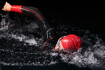 Image showing authentic triathlete swimmer having a break during hard training on night neon gel light