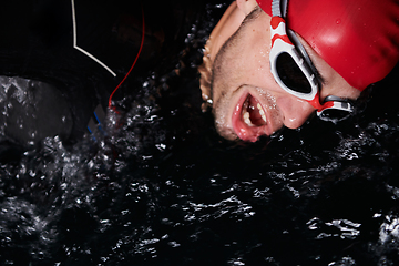 Image showing authentic triathlete swimmer having a break during hard training on night neon gel light