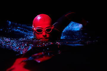 Image showing authentic triathlete swimmer having a break during hard training on night neon gel light