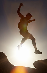 Image showing Man, silhouette and jump on rock at sunset with freedom, adventure and challenge on mountain or cliff. Climbing, hill and person with fearless leap in hiking, exercise or energy at with sky in summer